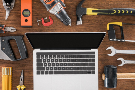 top view of workplace with laptop with blank screen surrounded by various tools on wooden tableの写真素材