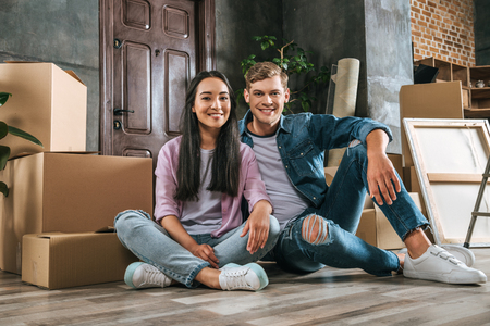 attractive young couple sitting on floor together while moving into new home