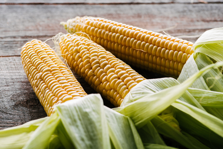 close up view of fresh raw corn cobs on wooden surfaceの写真素材