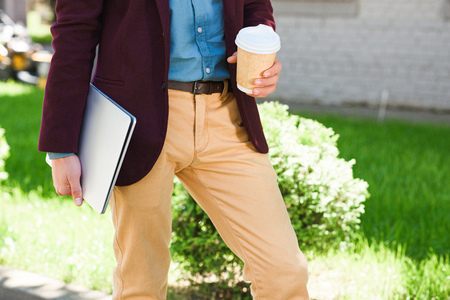 cropped shot of young man holding laptop and paper cup outsideの写真素材