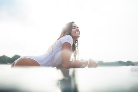 happy young woman lying on surfboard in ocean during summer vacation