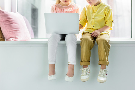 cropped shot of little kids sitting on windowsill and using laptopの写真素材