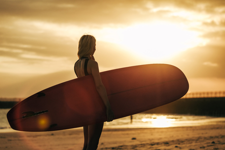 silhouette of surfer posing with surfboard on beach at sunset with back lightの写真素材
