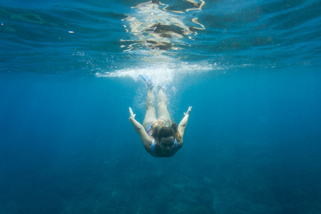 underwater photo of young woman in swimming suit diving in ocean aloneの写真素材