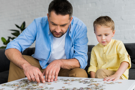 father and cute little son playing with jigsaw puzzle together at homeの写真素材