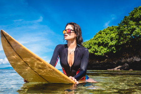 sportswoman in wetsuit and sunglasses on surfing board in ocean at Nusa dua Beach, Bali, Indonesiaの写真素材