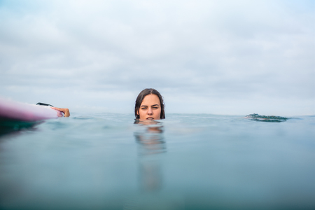 young woman swimming with surfboard on cloudy dayの写真素材