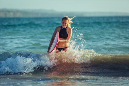 blonde female surfer with surfboard in waterの写真素材