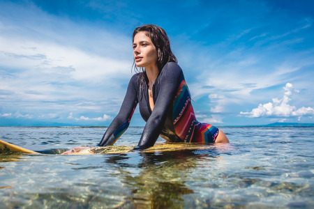 young sportswoman in wetsuit on surfing board in ocean at Nusa dua Beach, Bali, Indonesiaの写真素材