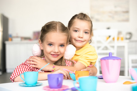 portrait of little smiling sisters pretending to have tea party together at homeの写真素材
