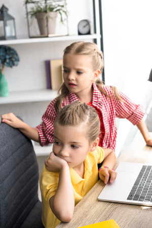 selective focus of little kids looking away at table with laptop at homeの写真素材