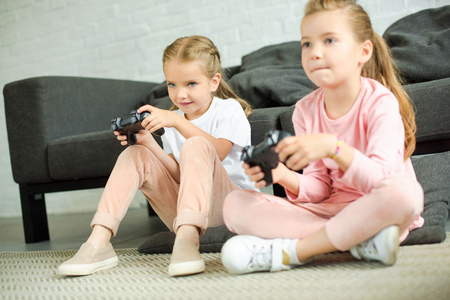 little sisters with gamepads playing video game together at homeの写真素材