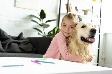 portrait of cute child hugging golden retriever dog near by at homeの写真素材