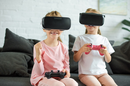 obscured view of kids in virtual reality headsets playing video game on sofa at home