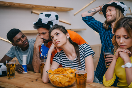 upset group of multiethnic friends in soccer ball hats watching football match at barの写真素材