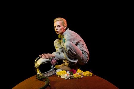 attractive alien in spacesuit with flowers and helmet sitting on planet