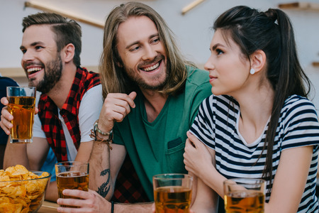 smiling group of friends drinking beer and watching football match at barの写真素材