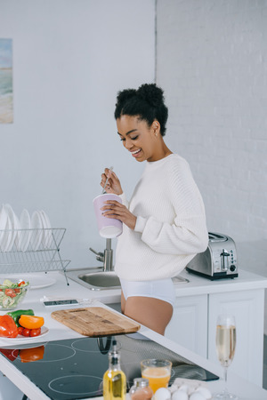 attractive young woman eating ice cream from bucket at kitchenの写真素材