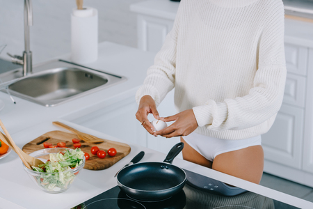 cropped shot of woman breaking eggshell to prepare  scrambled egg for breakfast at kitchenの写真素材