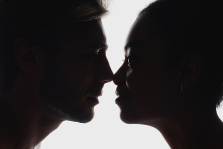 side view of silhouettes of interracial couple in love looking at each otherの写真素材