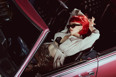 high angle view of stylish girl in trench coat and sunglasses lying with hands behind head in retro carの写真素材