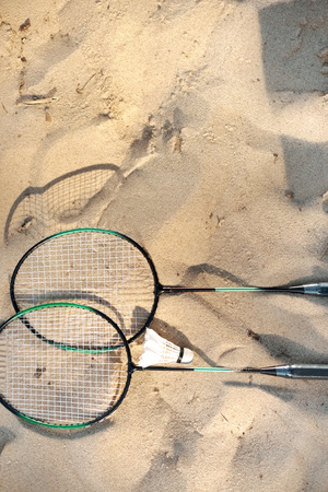 close up view of badminton racquets and shuttlecock lying on sandy beachの写真素材