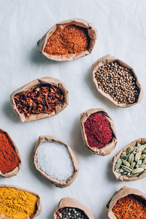 top view of colorful indian spices in paper bags on white tableの写真素材