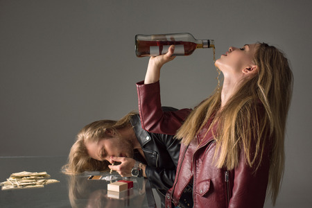 young addicted couple drinking alcohol and sniffing cocaine on greyの写真素材