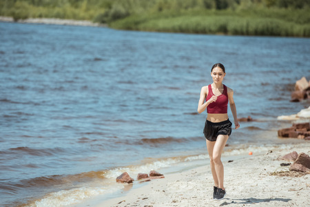 front view of young asian female jogger running on beach