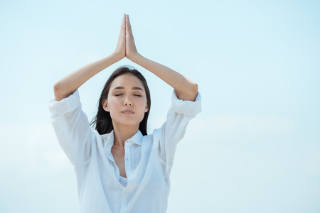 asian woman with closed eyes standing in asana vrikshasana (tree pose) against blue skyの写真素材