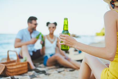 selective focus of group of friends with beer resting on sandy beach togetherの写真素材