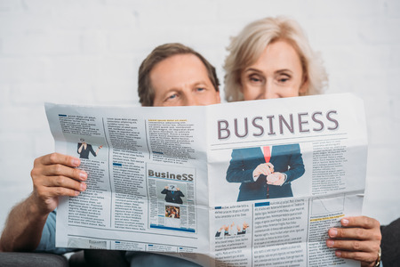 happy senior couple reading business newspaper together at homeの写真素材