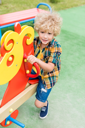 high angle view of happy curly boy riding on rocking horse at playgroundの写真素材