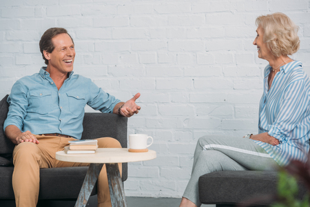 happy senior couple talking and smiling each other while sitting together at homeの写真素材