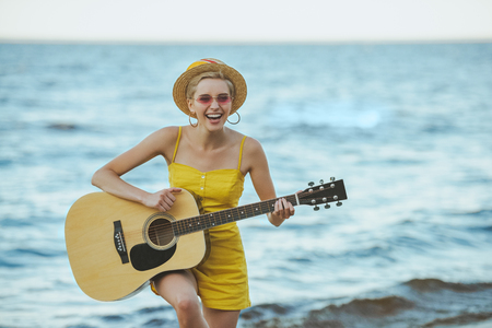 portrait of happy young woman playing guitar with sea on backgroundの写真素材