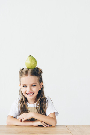 laughing little child with ripe pear on head isolated on whiteの写真素材