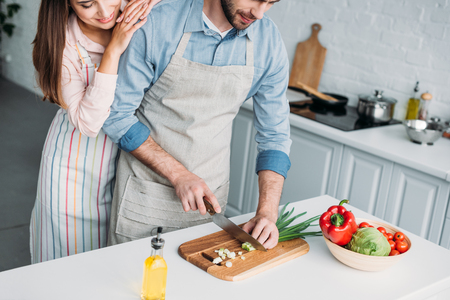 cropped image of boyfriend cutting vegetables and girlfriend leaning on him in kitchenの写真素材