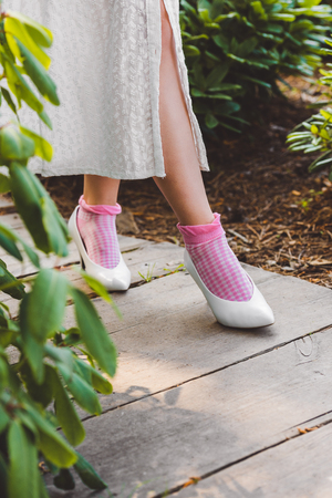 low section of girl in dress and stylish white shoes walking on wooden walkwayの写真素材