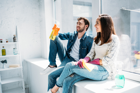 couple resting on windowsill after cleaning and having fun with spray bottle in kitchenの写真素材