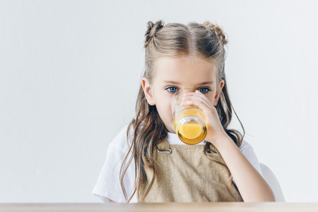 beautiful little schoolgirl with drinking orange juice isolated on white