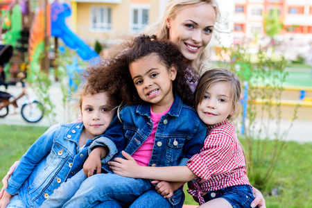 smiling mother with daughter and her multicultural friends sitting on benchの写真素材