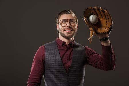 handsome smiling buisnesssman in eyeglasses holding ball with baseball glove isolated on blackの写真素材