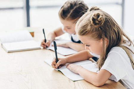 little schoolgirls writing in notebooks while doing homework isolated on whiteの写真素材