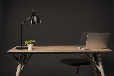 close up view of chair and table with lamp, plant, book and laptop on grey backgroundの写真素材