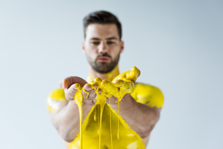 Handsome bearded man showing hands covered in yellow paint isolated on white backgroundの写真素材