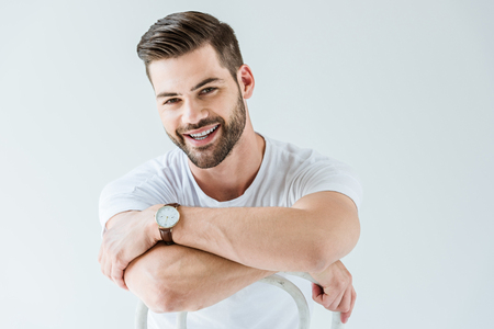 Fashionable confident man smiling while sitting on chair isolated on white backgroundの写真素材