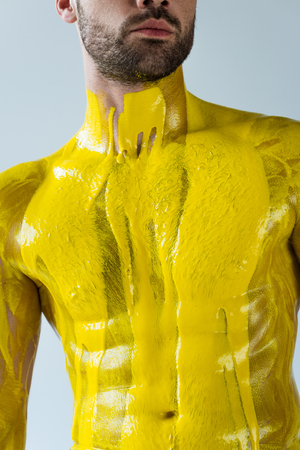 Yellow paint covering body of muscular man isolated on white backgroundの写真素材