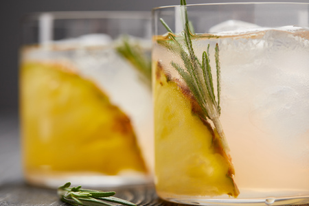 selective focus of two glasses of lemonade with pineapple pieces, ice cubes and rosemary on grey wooden tabletopの写真素材