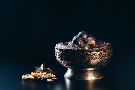 closeup view of vintage bowl with candies, chocolate pieces, nuts and dry orange slices on black backgroundの写真素材