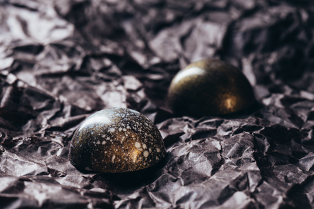 closeup shot of two chocolate candies with golden splashes on crumpled paperの写真素材
